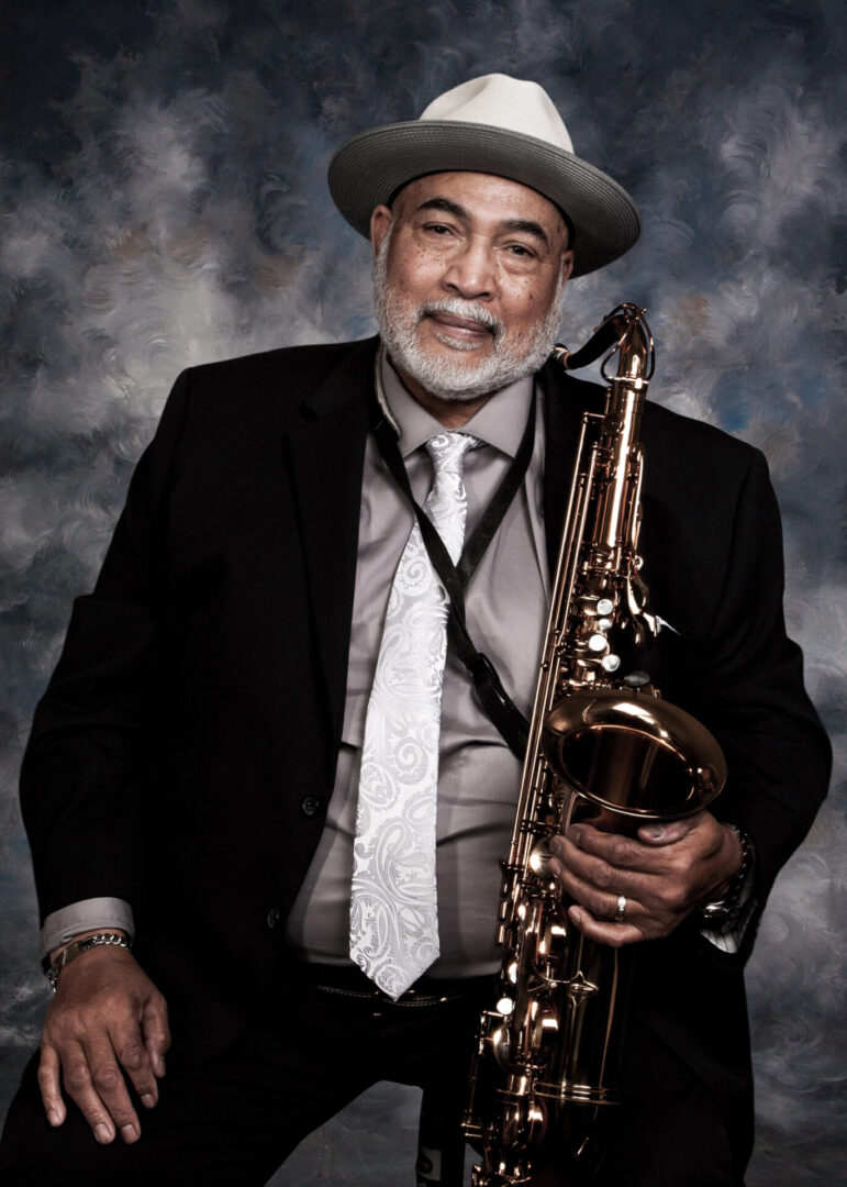 A man in a suit and hat holding a saxophone.